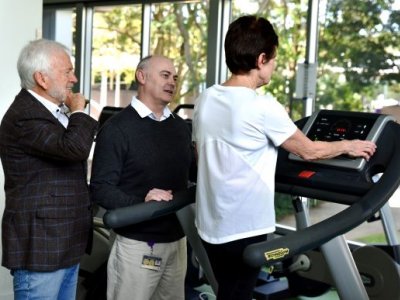Two people stand next to a person walking on a treadmill